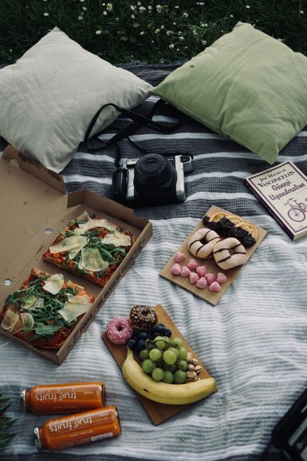 A picnic setup on a blue and white striped blanket laid on the grass in Brockwell Park, Brixton. The scene includes a pair of brown and white trainers, a container of green grapes, an art palette with